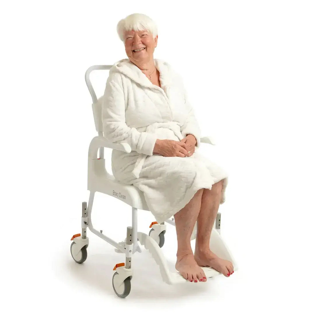 Woman in a white robe sitting on a white shower chair with wheels on a white background