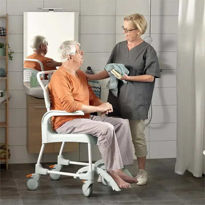 Etac Clean Rolling Shower Commode Chair from reliable ramps showing two people in bathroom using the chair