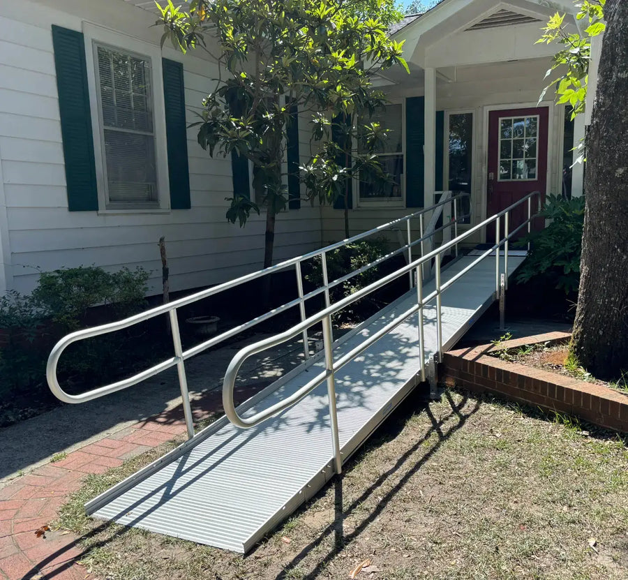 Metal wheelchair ramp leading to a house with a white exterior and green shutters.