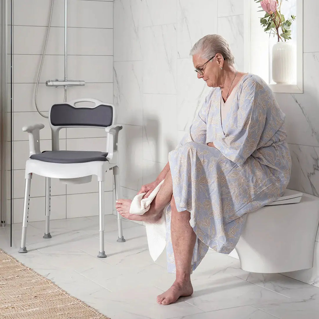 Woman sitting on a toilet with a shower chair in the background