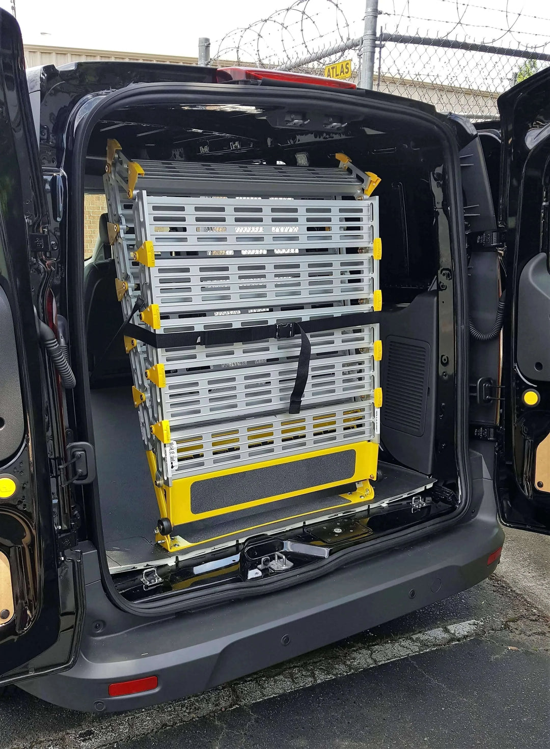 Roll-A-Ramp manual van ramp from Reliable Ramps folded up and strapped down in a black van