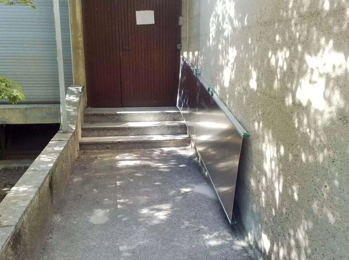 Guldmann - Stepless Wide Folding Portable Wheelchair Ramp folded up next to steps at a main entrance