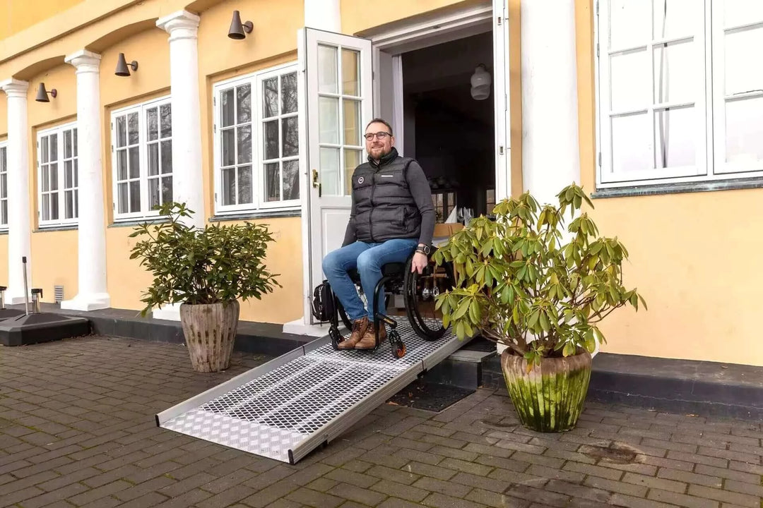 Guldmann - Stepless Wide Folding Pro Portable Wheelchair Ramp used by a patient coming out of a house