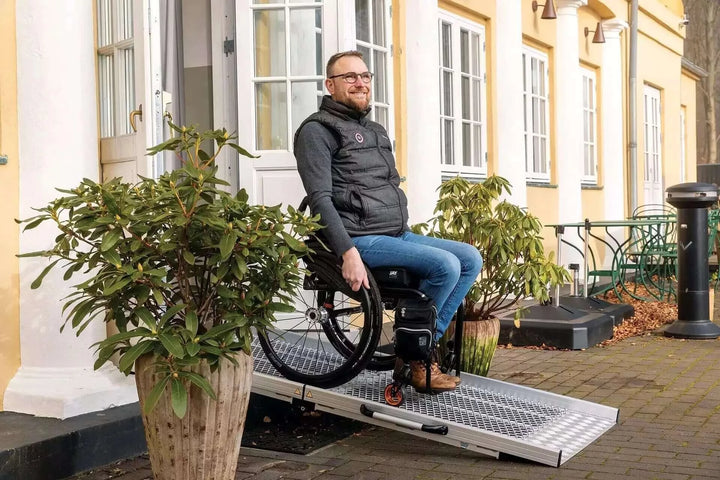 Guldmann - Stepless Wide Folding Pro Portable Wheelchair Ramp used by a patient coming out of a house