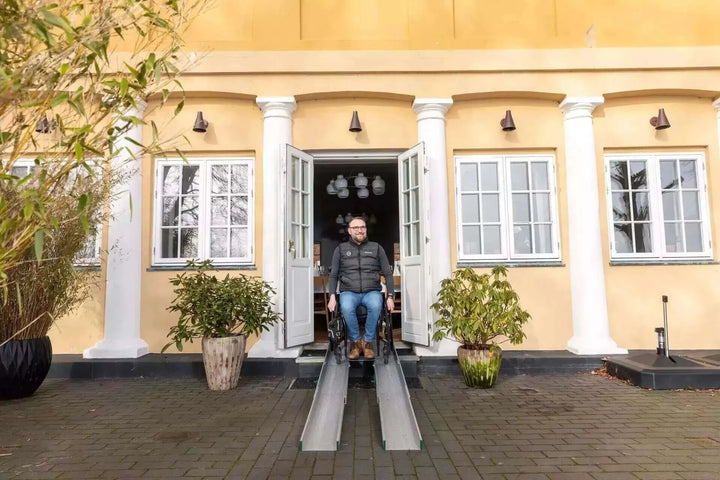 Guldmann - Stepless Folding Telescopic Portable Wheelchair Ramp being used by a man coming out of a building