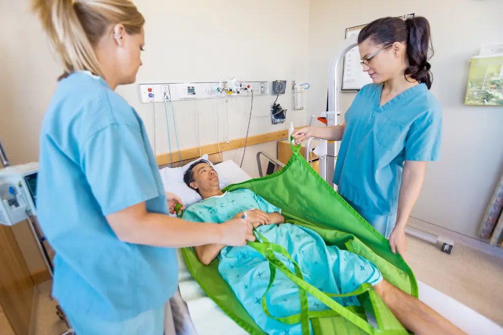 man laying in hospital bed with two nurses helping him into a green sling