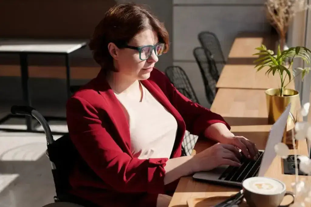 lady sitting at a computer at her desk while in a wheelchair wearing a white shirt and red jacket