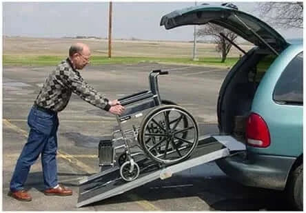 PVI - Aluminum Multi-Fold Rear Door Reach Portable Van Wheelchair Ramp being shown with a man pushing a wheelchair up it into a van.