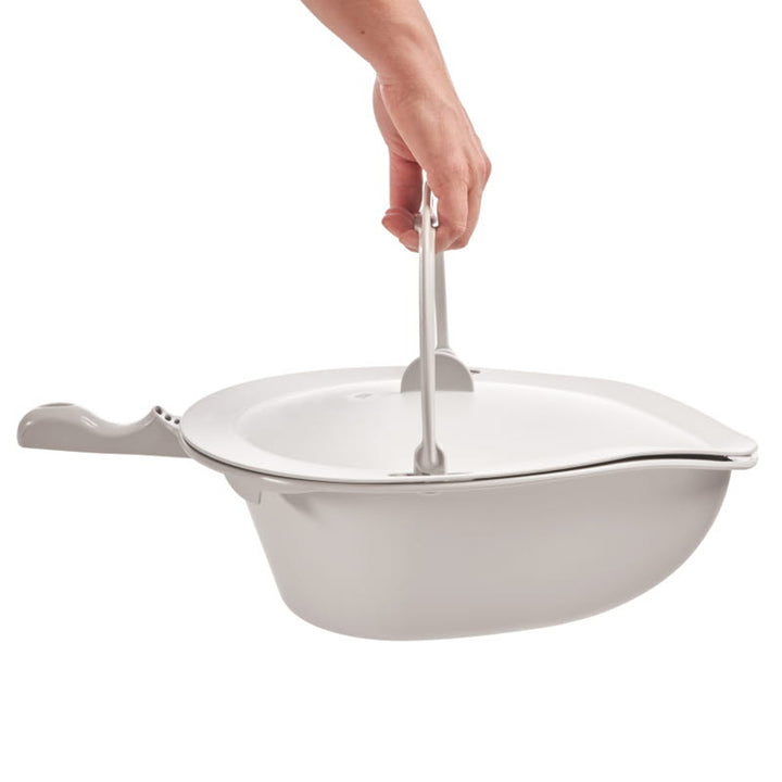 White ceramic dish with a lid and handle, held by a hand on a white background