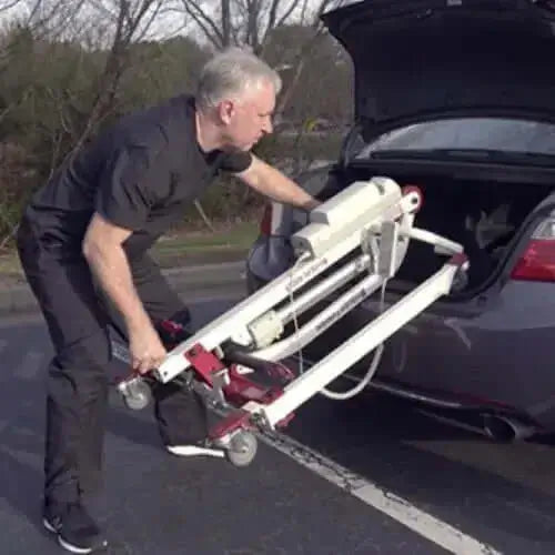 man putting a portable patient lift away in the trunk of a car