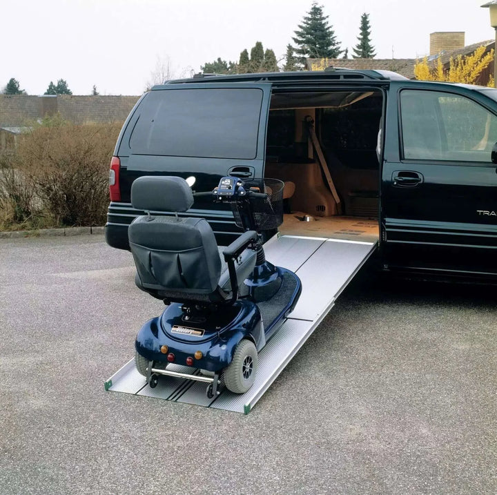 Guldmann - Stepless Telescopic EasyFold Wheelchair Van Ramp setup next to a minivan with an empty scooter on it
