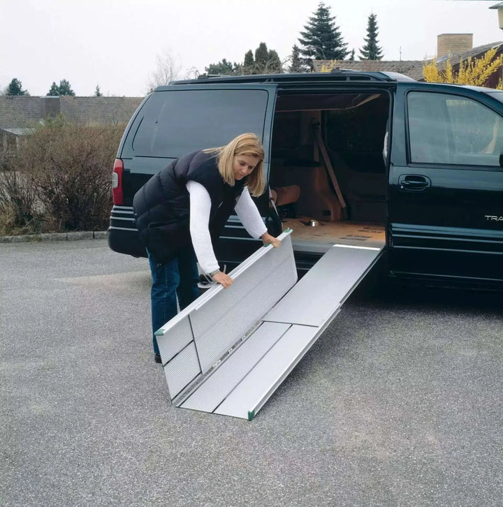 Guldmann - Stepless Telescopic EasyFold Wheelchair Van Ramp being folded up outside a van by a user