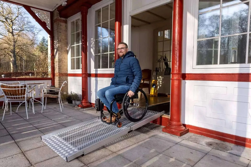 Guldmann - Stepless Wide Folding Pro Portable Wheelchair Ramp being used by user coming out of a home