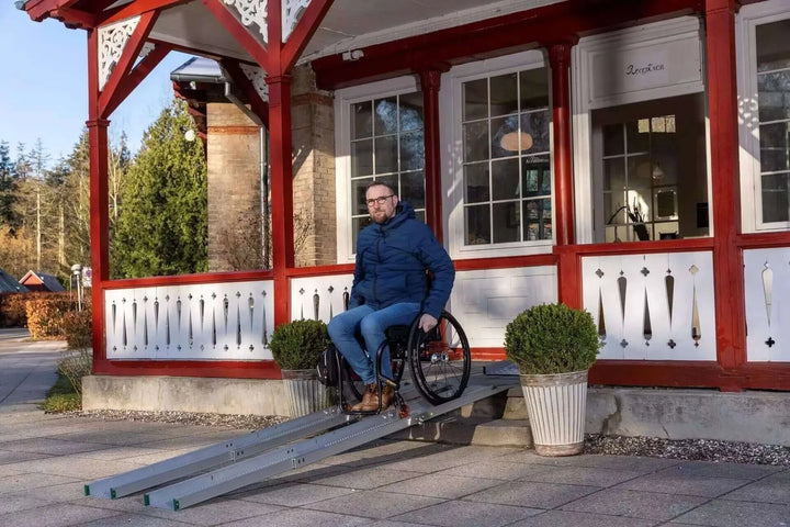 Guldmann - Stepless Folding Telescopic Portable Wheelchair Ramp being used by man coming out of house