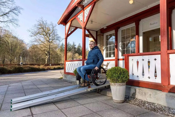 Guldmann - Stepless Folding Telescopic Portable Wheelchair Ramp being used by a man coming out of a house