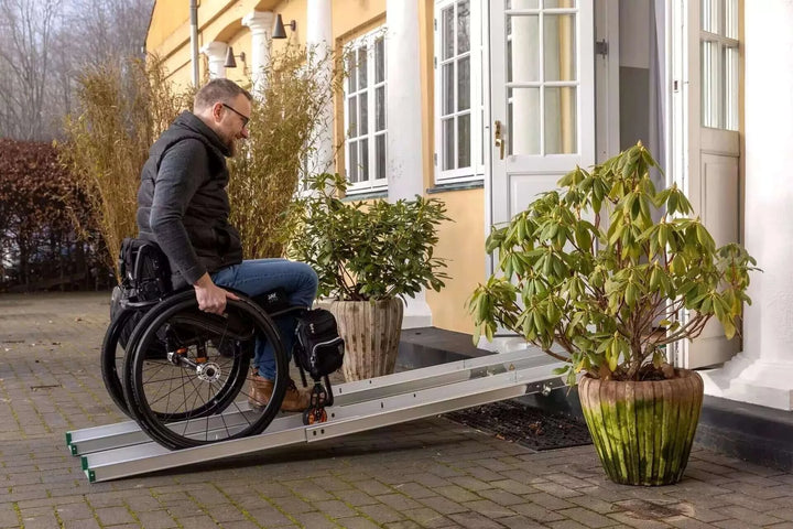 Guldmann - Stepless Folding Telescopic Portable Wheelchair Ramp being used by a man coming out of a building