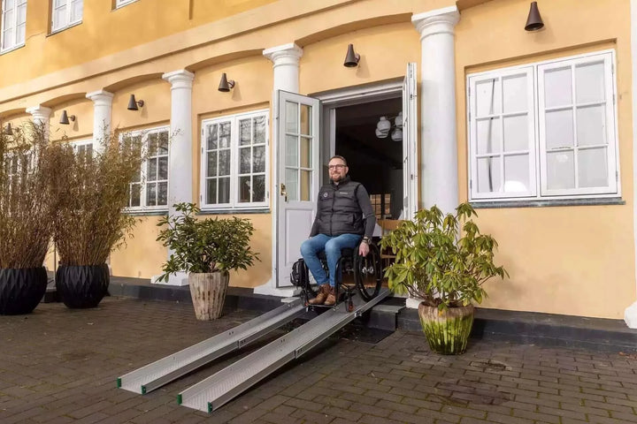 Guldmann - Stepless Folding Telescopic Portable Wheelchair Ramp being used by a man coming out of a building