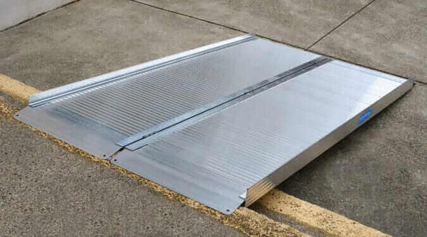 aluminum folding wheelchair ramp laid up against a curb