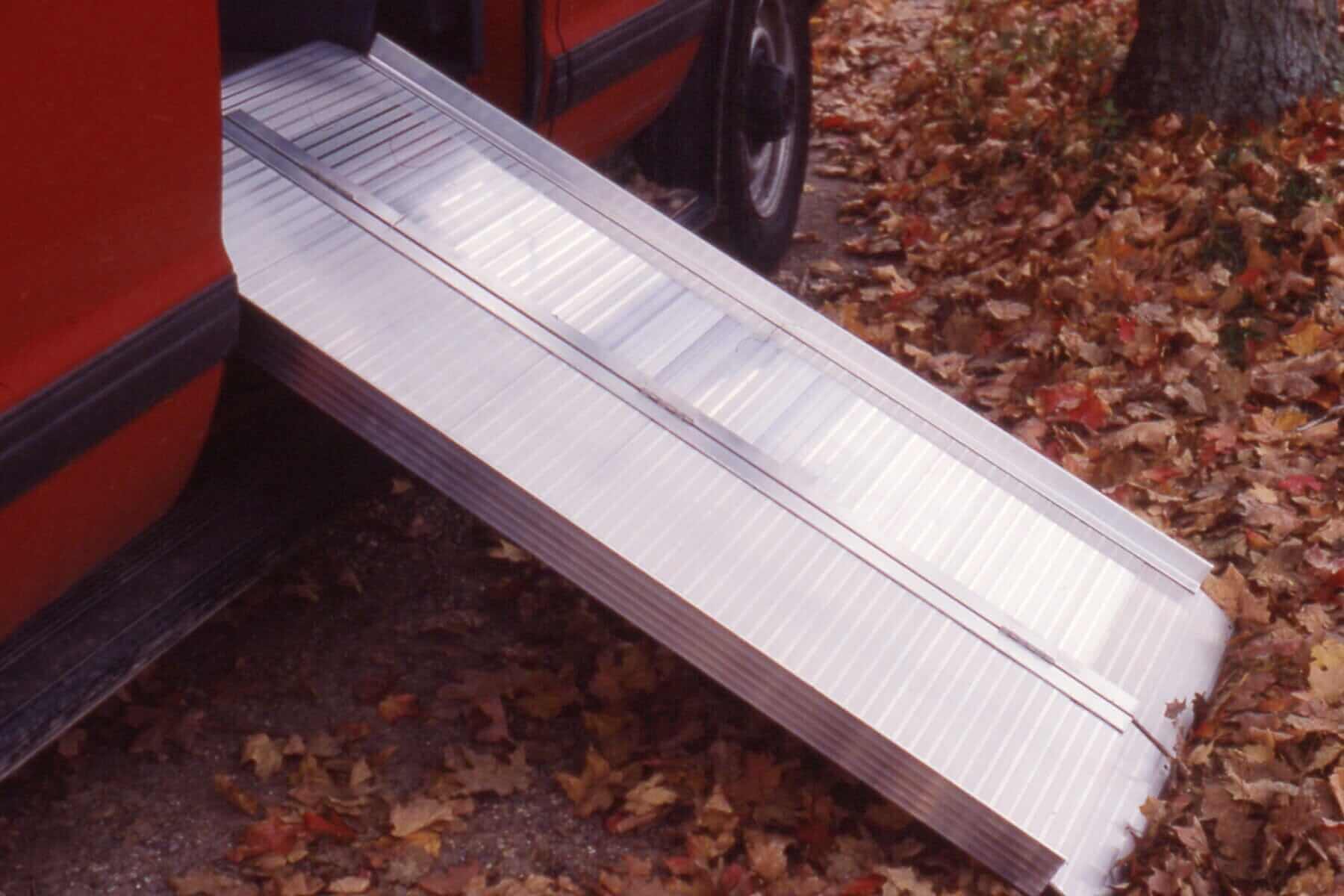 AlumiLite Folding Wheelchair Curb Ramp leaning up agains a red vehicle