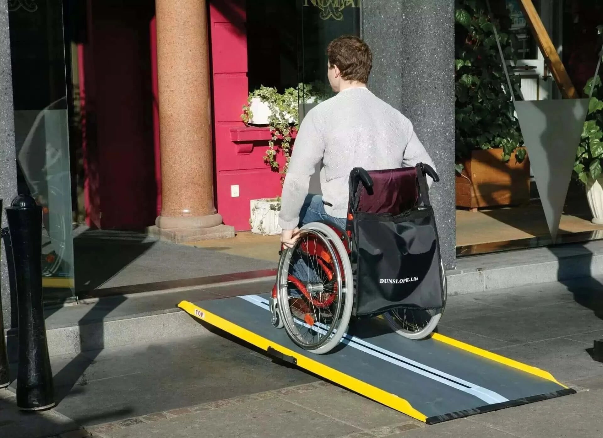 man going up fiberglass ramp up step in wheelchair outside